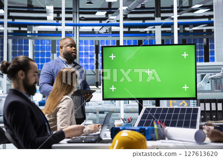 Photovoltaics factory management team monitoring system performance using isolated screen monitor. Solar panels manufacturing plant administrators tracking energy production using chroma key display Photovoltaics factory management team monitoring system performance using isolated screen monitor. Solar panels manufacturing plant administrators tracking energy production using chroma key display 127613620