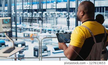 Photovoltaic smart factory engineer uses tablet to design production lines for assembly facility in CAD program. Industry 4.0 solar panels plant worker uses device to optimize floor layouts, camera A Photovoltaic smart factory engineer uses tablet to design production lines for assembly facility in CAD program. Industry 4.0 solar panels plant worker uses device to optimize floor layouts, camera A 127613653