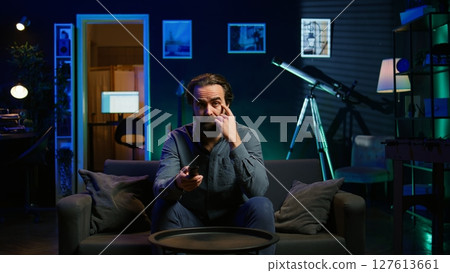 Perplexed supporter watching sports match on TV, surprised by unconvincing team performance. Man looking at football competition, baffled by easy chance missed by player, camera B closeup 127613661
