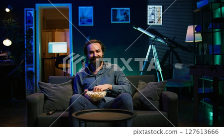Man in apartment chocking on food while watching movie on TV and eating popcorn. Person getting throat clogged while swallowing snack, doing heimlich maneuver on couch, fighting for his life, camera B 127613666