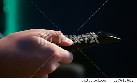 Close up of man in dimly lit apartment using remote control to browse though movies on streaming service. Remote control used by person in living room flipping through channels on TV, camera B Close up of man in dimly lit apartment using remote control to browse though movies on streaming service. Remote control used by person in living room flipping through channels on TV, camera B 127613692