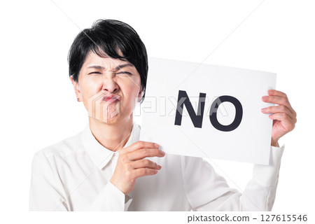 A middle-aged woman grimacing while holding a piece of paper with the word NO written on it 127615546