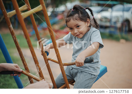 cheerful toddler girl playing on double swing with freind at outdoor playground 127617758