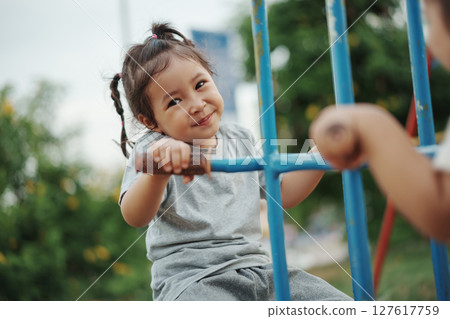 cheerful toddler girl playing on double swing with freind at outdoor playground 127617759