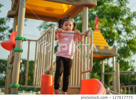 happy toddler girl hanging the bar by her hand at outdoor playground in park 127617773