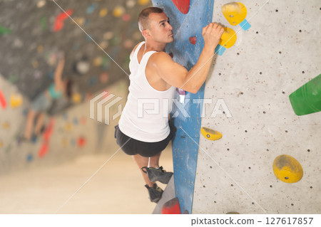 Young man climbing on artificial rock wall in rock-climbing gym 127617857