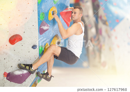 Young man climbing on artificial rock wall in rock-climbing gym 127617968