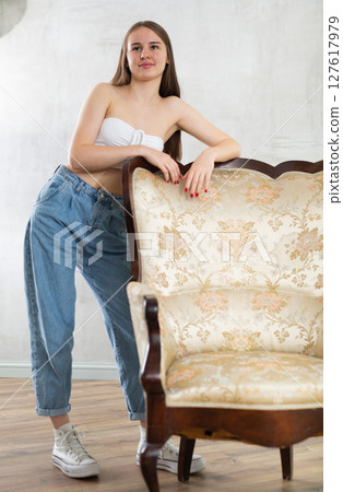 Portrait of a young positive girl next to luxury armchair 127617979