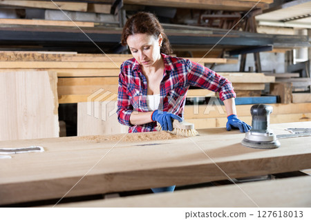 During manufacturing, woman employee grinds surface of wooden board, gives smoothness to surface 127618013
