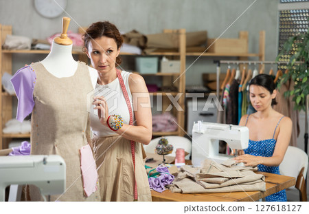Woman tailor connects parts of dress on mannequin, female craftsman tailor work and sewing 127618127