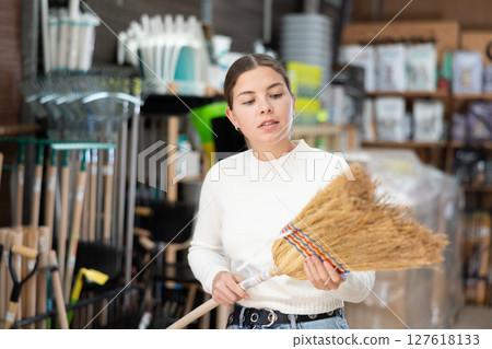 Young woman choosing broom in household store Young woman choosing broom in household store 127618133