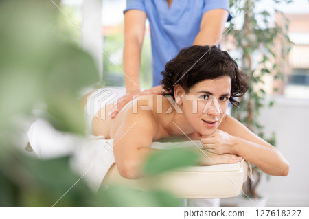 Masseur doing back massage to adult woman 127618227