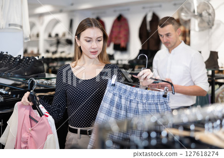 Girl holds hangers with blouses and skirt in her hands, selects comprehensive spring outfit. 127618274
