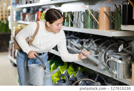 Amateur gardener girl selects watering can for her hobby in greenhouse flower-bed Amateur gardener girl selects watering can for her hobby in greenhouse flower-bed 127618286