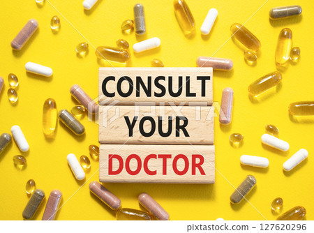 Consult Your Doctor symbol. Concept word Consult Your Doctor on wooden blocks. Beautiful yellow background with pills. Medicine and Consult Your Doctor concept. Copy space 127620296