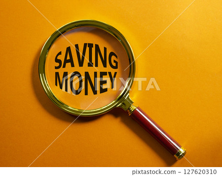 Saving Money symbol. Concept words Saving Money on magnifying glass. Beautiful orange background. Business and Saving Money concept. Copy space. Saving Money symbol. Concept words Saving Money on magnifying glass. Beautiful orange background. Business and Saving Money concept. Copy space. 127620310