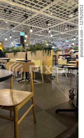 Interior of stylish restaurant with suspended wooden ceiling, partitions and plants, comfortable round tables with wooden chairs. 127620852