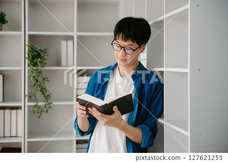 Male students note from the books at the Asian man library sitting at the desk using laptop computer and tablet to search an online informations. 127621253
