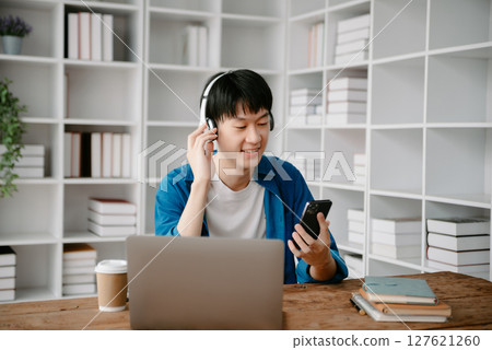 Smiling boy relaxing at home, she is playing music using smartphone tablet, laptop, and wearing white headphones. Smiling boy relaxing at home, she is playing music using smartphone tablet, laptop, and wearing white headphones. 127621260