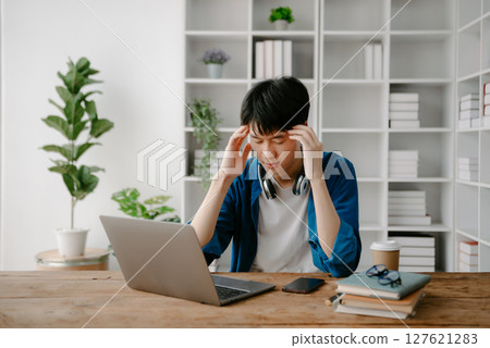 Male students note from the books at the Asian man library sitting at the desk using laptop computer and tablet to search an online informations. Male students note from the books at the Asian man library sitting at the desk using laptop computer and tablet to search an online informations. 127621283