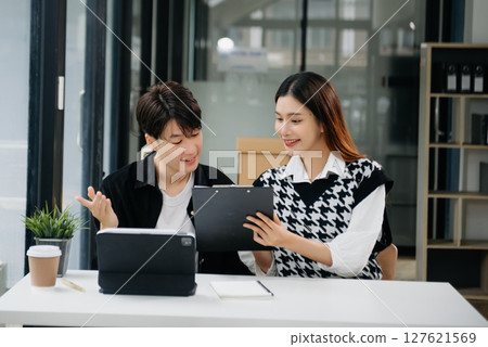 Two Asian businesswoman and man discuss investment project working and planning strategy with tablet laptop computer in office. Two Asian businesswoman and man discuss investment project working and planning strategy with tablet laptop computer in office. 127621569