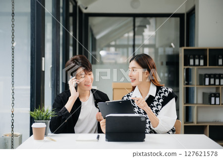 Two Asian businesswoman and man discuss investment project working and planning strategy with tablet laptop computer in office. Two Asian businesswoman and man discuss investment project working and planning strategy with tablet laptop computer in office. 127621578
