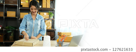 Banner Online seller Close up hands Young asian woman typing laptop keyboard checking online order on stock delivery package. Asian woman startup small business at home office with copy space 127621633