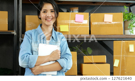 Asian woman startup small business at home office. Online seller entrepreneur young asian woman use tablet checking online order. Woman using tablet check stock goods supply delivery package shipping 127621640