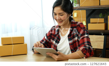 Asian woman startup small business at home office. Online seller entrepreneur young asian woman use tablet checking online order. Woman using tablet check stock goods supply delivery package shipping Asian woman startup small business at home office. Online seller entrepreneur young asian woman use tablet checking online order. Woman using tablet check stock goods supply delivery package shipping 127621643