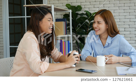 Two pretty best friends forever girlfriend talk, hug and laugh together sitting on sofa in cozy home relax. Happy friendship smile talking together positive emotion in living room joyful lifestyles 127621661