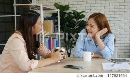 Two pretty best friends forever girlfriend talk, hug and laugh together sitting on sofa in cozy home relax. Happy friendship smile talking together positive emotion in living room joyful lifestyles 127621664