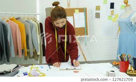 Entrepreneur fashion designer in textile business designing new retail clothing collection. Happy working woman seamstress, designer working on fabric sketches. Young designer fashion concept Entrepreneur fashion designer in textile business designing new retail clothing collection. Happy working woman seamstress, designer working on fabric sketches. Young designer fashion concept 127621709