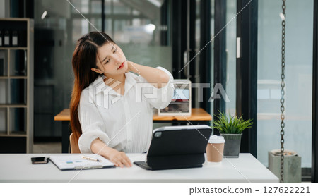 Overworked young Asian businesswoman office worker suffering from neck pain after had a long day at her office desk. office syndrome concept Overworked young Asian businesswoman office worker suffering from neck pain after had a long day at her office desk. office syndrome concept 127622221