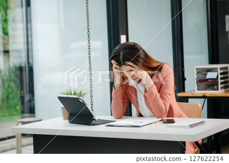 Asian business woman is stressed, bored, and overthinking from working on a tablet at the modern office. 127622254