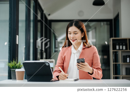 Asian businesswoman working in the office with working notepad, tablet and laptop documents Asian businesswoman working in the office with working notepad, tablet and laptop documents 127622256