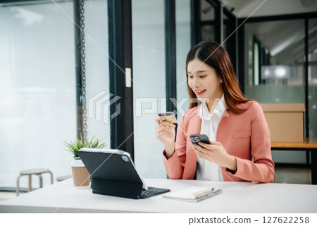 Woman using smart phone for mobile payments online shopping, omni channel, sitting on table, virtual icons graphics interface screen Woman using smart phone for mobile payments online shopping, omni channel, sitting on table, virtual icons graphics interface screen 127622258