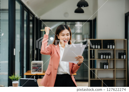 Confident Asian woman with a smile standing holding notepad and tablet at the modern office. 127622274