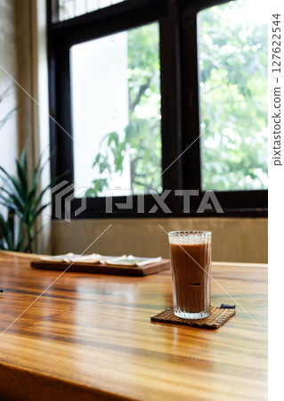Cup of delicious iced chocolate on wooden table background by the window. Cup of delicious iced chocolate on wooden table background by the window. 127622544