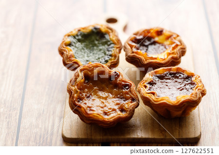 Stack of assorted Portuguese sweet dessert egg tart or Pastel de Nata on wooden board on wooden table. 127622551
