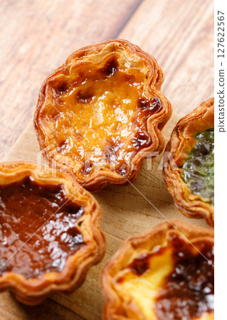 Stack of assorted Portuguese sweet dessert egg tart or Pastel de Nata on wooden board on wooden table. 127622567
