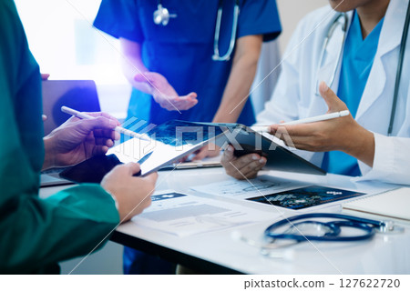 Medical team having a meeting with doctors in white lab coats and surgical scrubs seated at a table discussing a patients working online using computers Medical team having a meeting with doctors in white lab coats and surgical scrubs seated at a table discussing a patients working online using computers 127622720