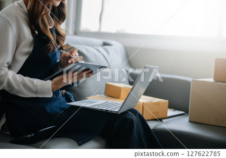 Woman hand using a laptop, smartphone and tablet and writing notebook at the office of her business online shopping. In home 127622785