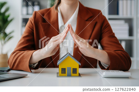 Female real estate agent is use hands to protect red roof for the concept of real estate investment about house trading, purchase at desk in office Female real estate agent is use hands to protect red roof for the concept of real estate investment about house trading, purchase at desk in office 127622840