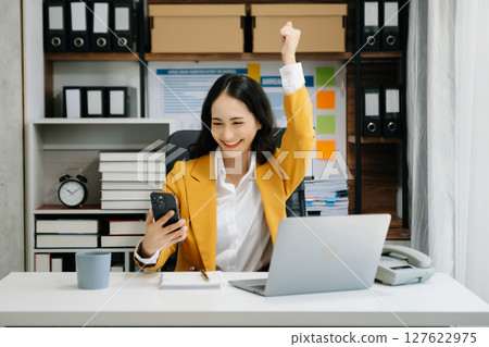 Asian business woman are delighted and happy with the work they do on their tablet, laptop and taking notes at the office. 127622975