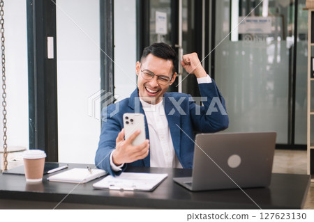 Young handsome man typing on tablet and laptop while sitting at the working wooden table modern office 127623130