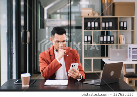 Young handsome man typing on tablet and laptop while sitting at the working wooden table modern office Young handsome man typing on tablet and laptop while sitting at the working wooden table modern office 127623135