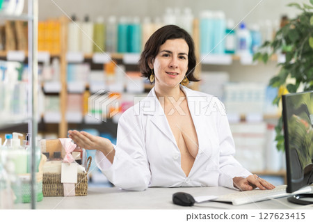Female pharmacist in unbuttoned gown invites to pharmacy 127623415