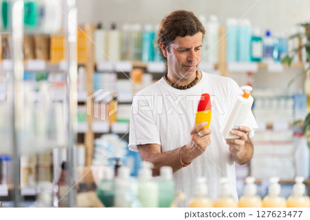 Adult man chooses sunscreen at pharmacy 127623477