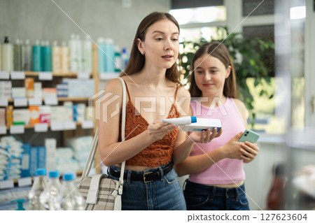 Woman with teen girl are busy choosing ointment for bruises at pharmacy Woman with teen girl are busy choosing ointment for bruises at pharmacy 127623604