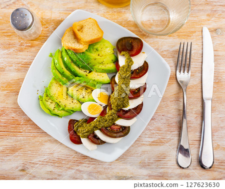 Slices of mozzarella and tomatoes - Italian salad caprese with addition boiled eggs and avocado 127623630